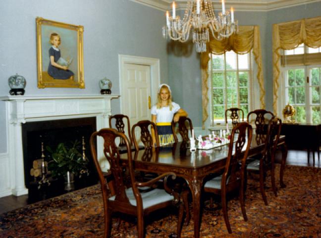 The Carr’s Hill dining room during the Shannon administration. Eleanor Shannon is the subject of the portrait over the fireplace. Lois Shannon stands by the table.